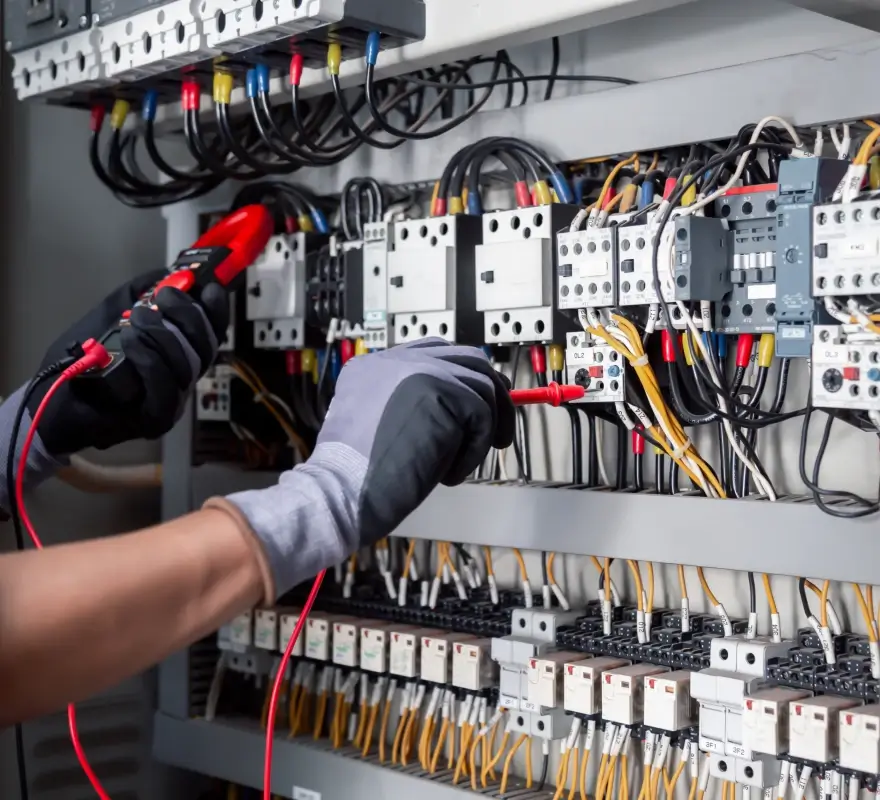 Electrician testing motor starter components inside an industrial control panel